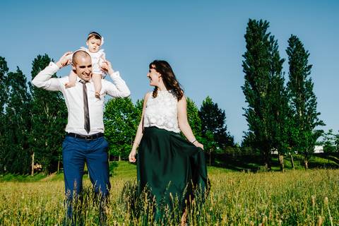 pai caminha com a criança ao colo no dia do baptizado e a mãe caminha ao lado'