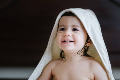 criança sorri sentada na cama depois do banho'