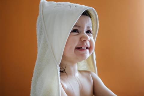 criança sorri sentada na cama depois do banho'