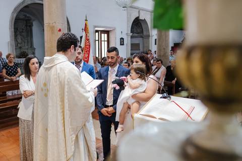 o padre reza enquanto os pais seguram a criança no colo'