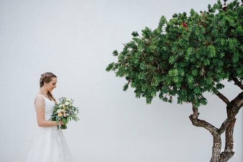 Noiva segura o bouquet junto a árvore de sua casa.'