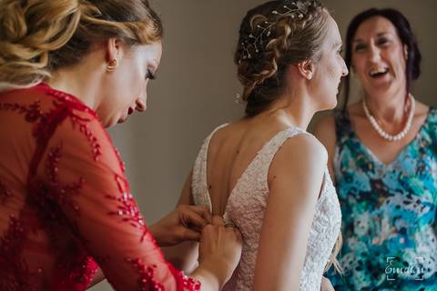Mãe e irmã ajudam a noiva a vestir-se.'