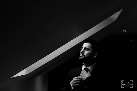 Noivo ajeita a gravata à janela do quarto.'