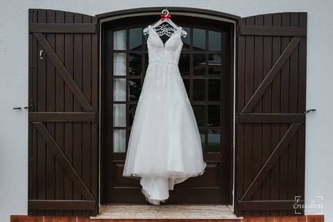 Vestido da noiva pendurado na janela do quarto.'