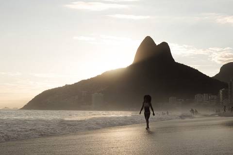Morro Dois Irmãos ao fundo com menina na praia de Ipanema ao entardecer'