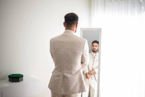 Fotografia de noivo a olhar-se ao espelho enquanto se prepara para o casamento'