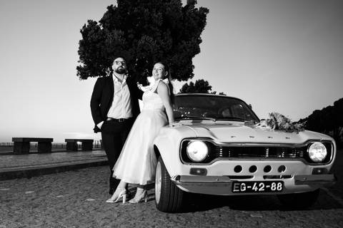 casal encostado a um carro a olhar para o céu - fotografia de pré-wedding a preto e branco'