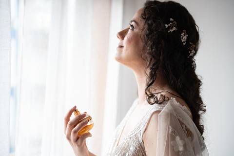 fotografia de noiva a pôr perfume em frente à janela no dia do casamento'