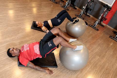 Exercício de core com bola suíça durante treino funcional na academia'