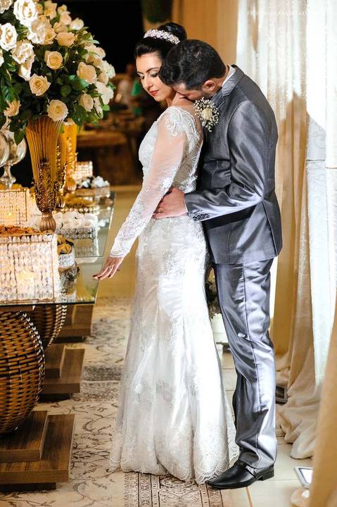 Fotografia dos noivos na recepção do casamento, foto de noivos lindos, foto de casamento atrás da mesa de doces, fotografia de casal se abraçando'