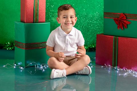 Cenário de natal decorado com presentes, com menino de 3 anos sentado e sorrindo'
