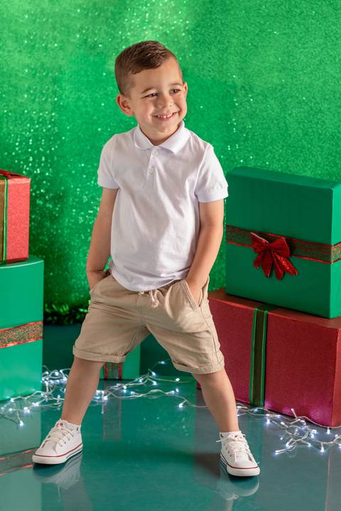 Cenário de natal verde decorado com presentes, com menino de 3 anos em pé e sorrindo'