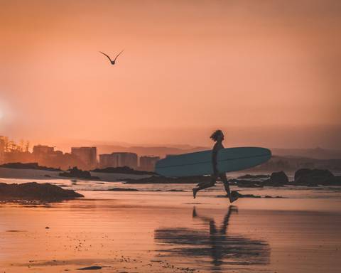 Homem segurando uma prancha de surf na praia no por do sol em Rainbow Bay'