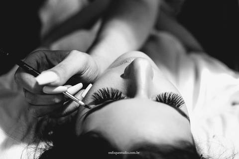 Fotografia em preto e branco da noiva Gabriela sendo maquiada e colocando cílios no Hotel Plaza, Itu'
