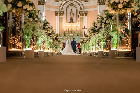Visão dos Noivos ajoelhados através do corredor decorado da Igreja do Quartel, em Itu, durante a cerimônia de casamento'