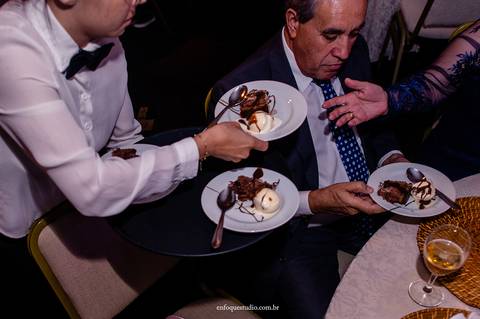 Fotografia espontânea do bolo de casamento de Gabriela e Guilherme sendo distribuído na recepção em Itu.'