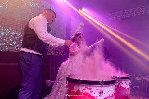 Casal de noivos participa do show de percussão iluminada, tocando tambores com pó colorido na festa em Itu.'