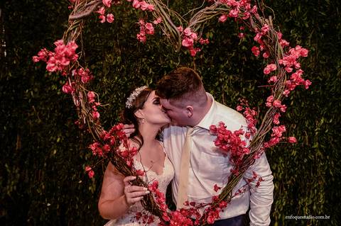 Noivos Gabriela e Guilherme se beijando no arco de flores em formato de coração durante a festa de casamento em Itu'