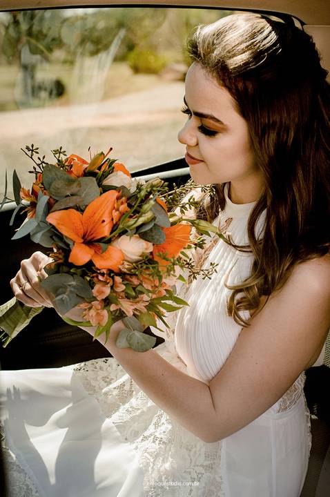 A noiva segura o buquê e contempla o momento antes da cerimônia, transmitindo delicadeza e emoção no dia do casamento.'