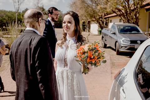 A noiva é recebida com carinho pelos pai logo ao descer do carro, um instante de afeto antes da cerimônia.'