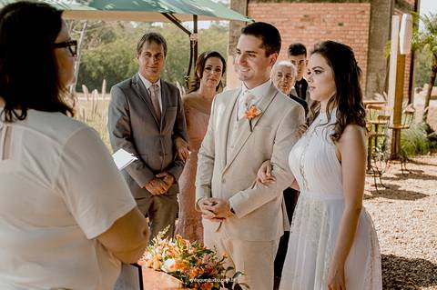 O casal inicia a cerimônia ao ar livre, lado a lado, cercados por familiares e amigos próximos.'