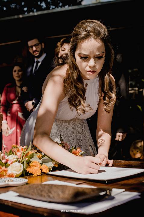 A noiva registra sua assinatura no livro oficial, selando o compromisso diante da família e amigos.'