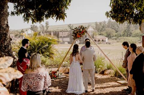 De mãos dadas, os noivos observam o altar decorado em meio à natureza, vivendo um cenário cheio de significado.'