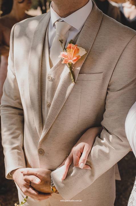 Detalhe do traje do noivo em tom claro, com flor na lapela, enquanto recebe o carinho da noiva durante o casamento intimista em Piracicaba.'