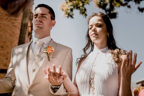 De mãos dadas, os noivos elevam um instante de fé e oração no casamento ao ar livre em Piracicaba.'