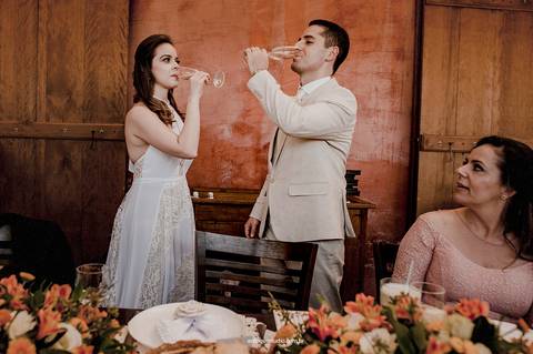 O primeiro brinde como casal, cercado por quem importa, marcando o início de uma nova fase.'