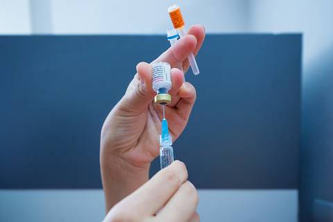 Fotografia publicitaria e institucional de uma enfermeira preparando uma vacina.'