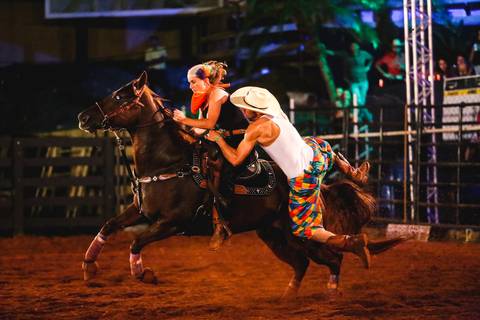 Fotografia de evento rural onde peão tenta subir no cavalo em prova chamada Mala de Loucos'