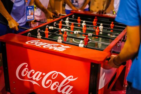 Atletas dos Jogos Escolares da Juventude se divertem em mesa de pebolim, a fotografia corporativa valorizando a marca.'