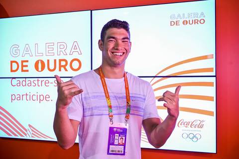 Atleta posa para fotografia corporativa em frente a painel publicitário da Coca Cola.'