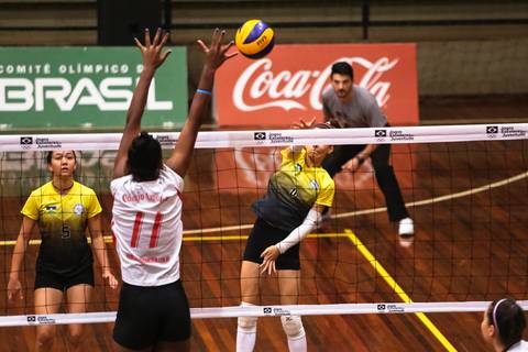 Fotografia esportiva de uma disputa de vôlei valorizando placa de publicidade da Coca Cola.'