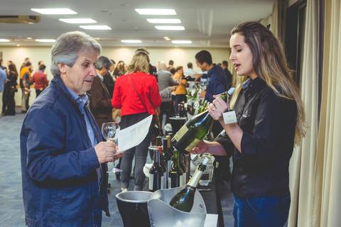 Fotógrafo profissional de Londrina faz imagem de uma jovem enóloga mostrando uma garrafa de vinho a empresário durante degustação de vinhos finos.'