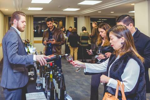 Imagem de fotógrafo em Londrina mostra um enólogo da Enoteca Decanter servindo vinho a comerciantes durante degustação.'