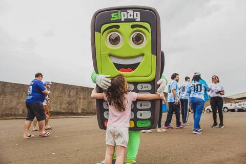 Menina abraça mascote Zipaguito, em fotografia de evento corporativa no Estádio do Café em Londrina-PR.'