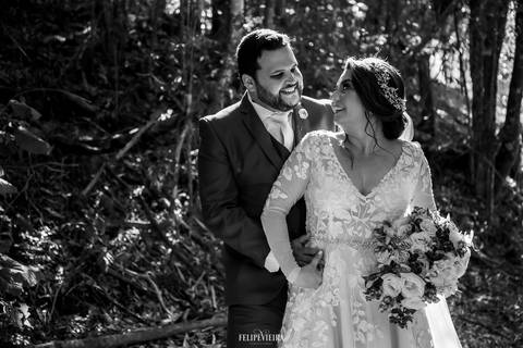Retrato em preto e branco de noivos abraçados e sorrindo em ensaio externo em Pedra Azul, com detalhes do buquê da noiva'