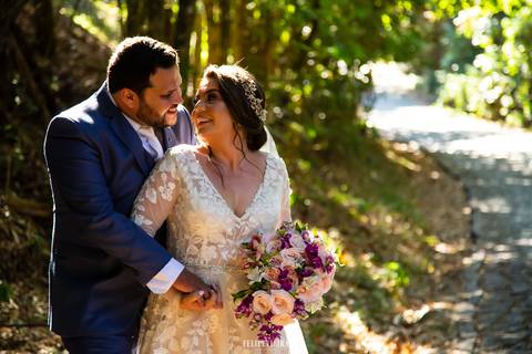 Retrato de noivos abraçados e se olhando com detalhes do vestido de noiva e buquê enquanto se olham e sorriem em ensaio externo pós-wedding'