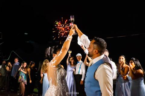 noivos brindando em festa de casamento em guarapari com fogos de artifício'