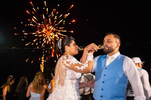 Noivos brindando com fogos de artifício ao fundo em sua festa em guarapari'