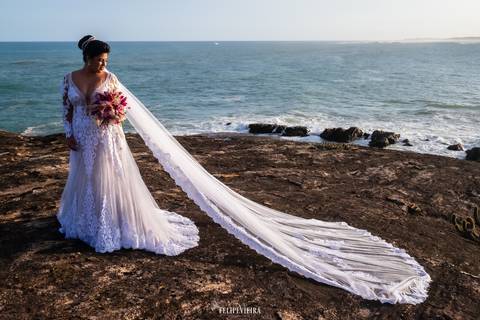 Noiva com buquê em frente ao mar em ensaio ao pôr do sol'