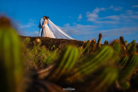 Noivos de mãos dadas em rochas sob o céu azul em ensaio externo pós-wedding'