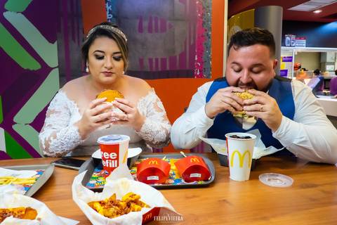 noivos no McDonalds com o noivos mordendo um bigmac e a noiva se preparando para morder o dela no final do ensaio pós wedding'