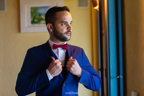 retrato do noivo segurando o terno em frente a uma janela'