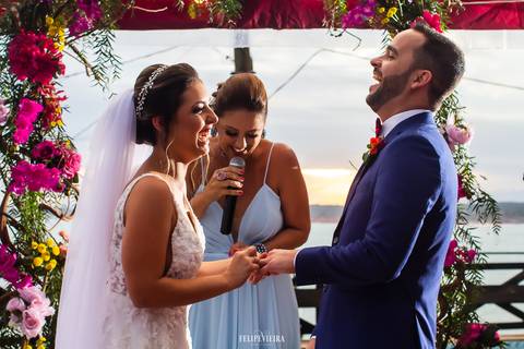 troca de alianças com os noivos sorrindo durante cerimônia fim de tarde'