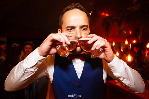 noivo durante a festa se divertindo com dois copos de cerveja na boca'
