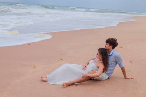 Noivos rolando na areia, rindo e vivendo o momento. Um ensaio que mostra que o verdadeiro amor também se diverte.'