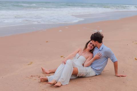 Noivos rolando na areia, rindo e vivendo o momento. Um ensaio que mostra que o verdadeiro amor também se diverte.'
